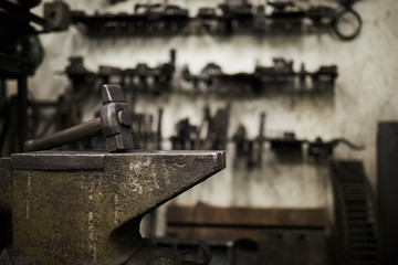 Heavy hammer on iron anvil and set of handtools of blacksmith on background