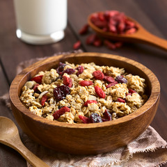 Crunchy oatmeal cereal with almond and dried goji berries and cranberries in wooden bowl, photographed with natural light (Selective Focus, Focus in the middle of the bowl)