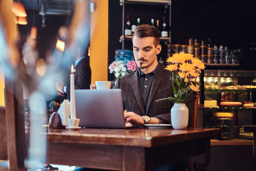 Handsome freelancer man with stylish beard and hair dressed in a black suit working on laptop while sitting at a cafe.