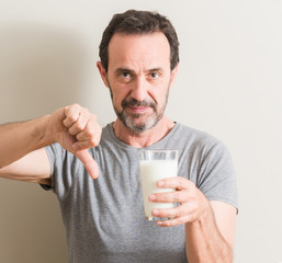 Senior man drinking a glass of milk with angry face, negative sign showing dislike with thumbs down, rejection concept