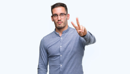 Naklejka premium Handsome young elegant man wearing glasses smiling looking to the camera showing fingers doing victory sign. Number two.