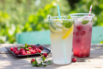 SOFT DRINKS. Refreshing summer drink lemon with mint, ice and raspberry with basil, ice. Glasses with cold and healthy beverage in a rustic style. Copy space.