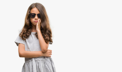 Brunette hispanic girl wearing sunglasses thinking looking tired and bored with depression problems with crossed arms.