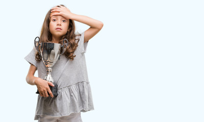 Brunette hispanic girl holding a trophy stressed with hand on head, shocked with shame and surprise...