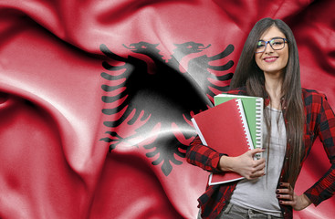 Happy female student holdimg books against national flag of Albania