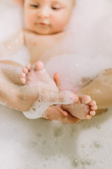 Happy laughing baby taking a bath playing with foam bubbles. Little child in a bathtub. Infant washing and bathing. Hygiene and care for young children. Adorable bath baby with soap suds on hair