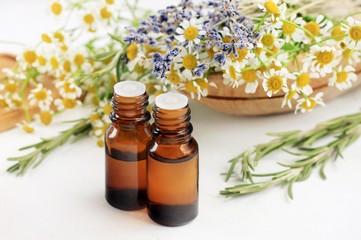 Essential oil blend with different aroma herbs: chamomile, rosemary, lavender. Fresh blossom and droppper bottles white table. Healing aromatherapy. - obrazy, fototapety, plakaty