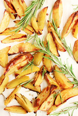 Oven baked potatoes with rosemary aromatic herb, oil, sprinkled sea salt. Top view golden roasted crisp vegetable slice,beige baking paper sheet. 