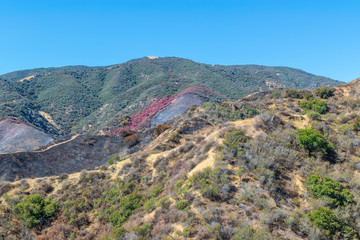 Southwest mountains after forest fire with burned hills and red fire retardant covering hillsides to stop the spread of fire