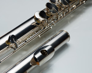 A silver bass flute lying on a white reflective surface