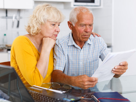 Worried mature couple with documents near laptop in home