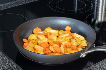 pan on a modern stove with carrots and potatoes in it. cooking in the kitchen