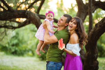 Happy family in the park evening light. Mom, dad and baby happy walk at sunset.