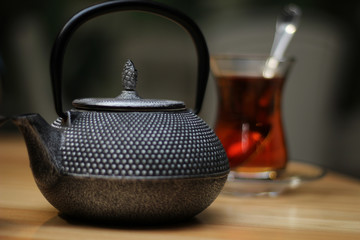 glass of black tea with spoon and kettle on wooden table