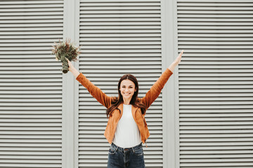 Positive and happy girl is looking on camera and smiling. She is holding hands up. Girl has flowers in hand. Isolated on striped and white background