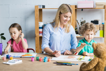 Young woman crafting together with her children sitting at wooden drawing table