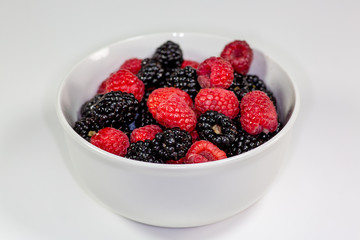 A white bowl with a mixture of raspberries and blackberries on a kitchen table waiting to be eaten 