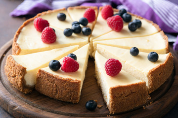 Classic plain New York Cheesecake with fresh berries sliced on wooden board. Closeup view
