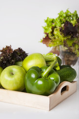 Fresh green vegetables and fruits in wooden boxes on white background. Bell pepper, apples, zucchini, celery, salad leaves.