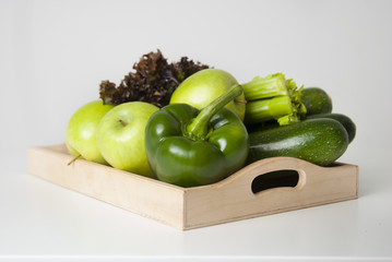 Fresh green vegetables and fruits in wooden boxes on white background. Bell pepper, apples, zucchini, celery, salad leaves.