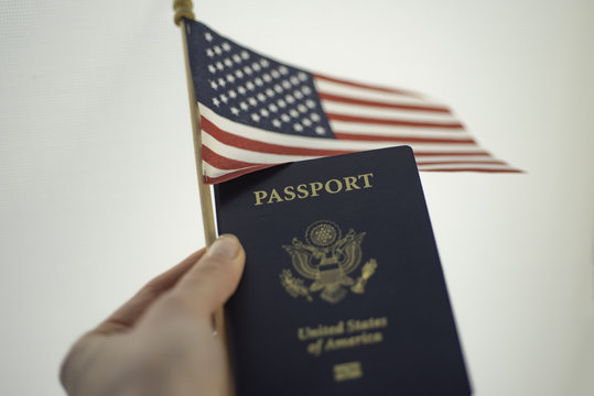 Holding Passport of USA and American flag in left hand, white background.