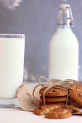 cookies with milk on wooden table and dark back. fresh milk and broken oat cookie with bow