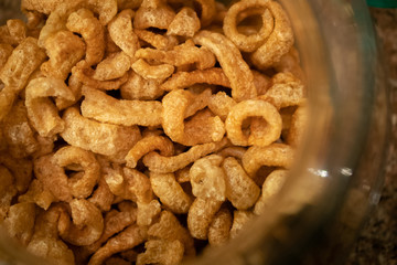 Chicharron or crispy fried pork rinds crackling in a jar. It's a delicious and nutritious snack but because of high in sodium and fat, it is very fattening and bad for your health. Warm light.