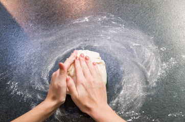 Woman preparing pizza dough on black granite table