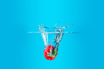 A fresh and delicious red strawberry isolated on a blue background. Red strawberry dropping in water and creating a splash. The concept of healthy eating, consuming fruit.