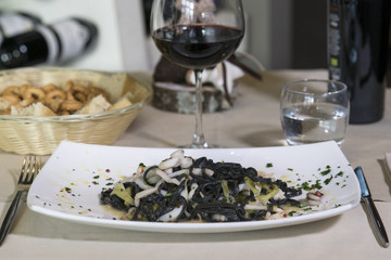 piatto di linguine al nero di seppie ccon frutti di mare servito in un ristorante con un calice di vino nero