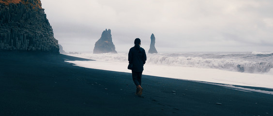 Woman walking alone on black sand beach at Reynisfjara, Iceland. 