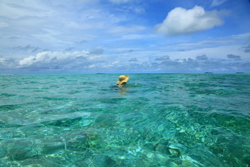 Gorgeous view of Indian Ocean, Maldives. Woman in hat swimming. Turquoise water surface and blue sky with white clouds. Beautiful backgrounds. 