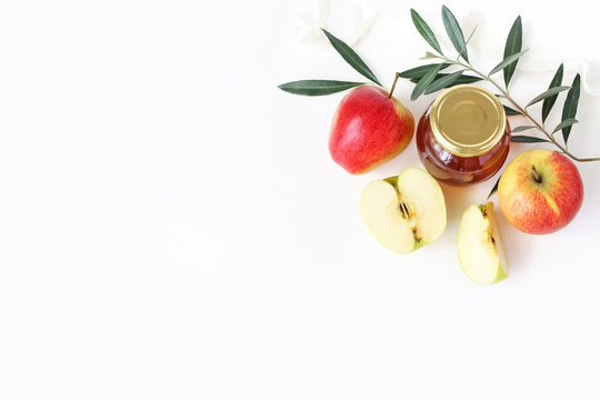 Rosh hashana, Jewish New Year greeting card, invitation. Food styled stock composition with honey jar, apples, olive branch and ribbon isolated on white table background. Flat lay, top view.