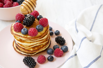 Tasty pancakes with berries and honey on a pink plate, side view. Closeup.