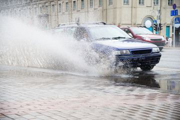 spray from a blue car from a puddle in the rain on the road with lens flare