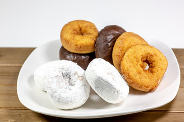 An assortment of donuts, powder donuts, chocolate donuts and plain donuts and a table waiting to be eaten