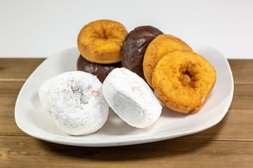 An assortment of donuts, powder donuts, chocolate donuts and plain donuts and a table waiting to be eaten