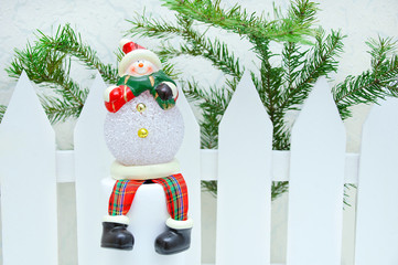 Christmas home decor. Toy snowman near a white fence with a Christmas tree.