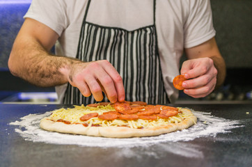 Obraz na płótnie Canvas Man preparing pepperoni pizza on black granite table