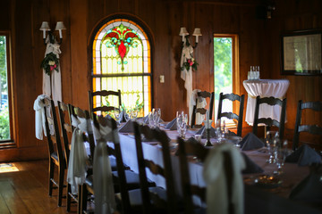 Fototapeta na wymiar Intimate Wedding Reception Table Setting with White Table Cloth in a Wood Panel Restaurant Room with Stained Glass Window and Chandelier