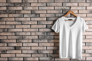 Hanger with blank t-shirt on brick wall. Mockup for design