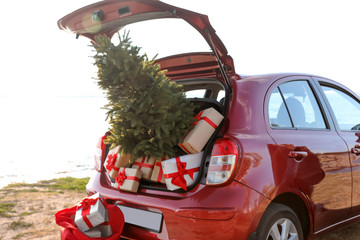 Fototapeta premium Red car with gift boxes and Christmas tree on beach. Santa Claus delivery
