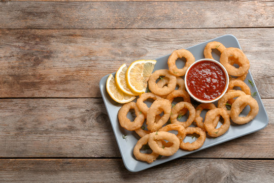 Fried onion rings served with sauce and lemon slices on plate, top view