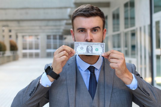 Businessman with dollar bill covering mouth 