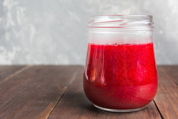 Red berries sause or jam in glass jar on wooden table