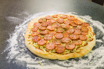 Preparing pepperoni pizza on black granite table