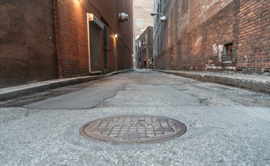 Low angle site of long Europe style back alley way in Cleveland, Ohio with view of man hole cover.