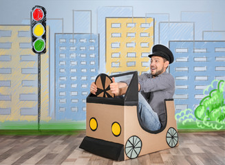 Young man dreaming of buying own auto while playing with cardboard car indoors