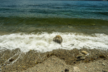 white waves pounding the small rock on the sandy beach