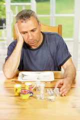 Caucasian man, alone, sit at a table, day, worrying about the pills he is supposed to take.